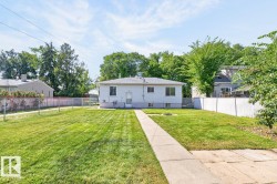 Expansive backyard featuring a manicured lawn, concrete pathway, and mature trees, enclosed by a chain link fence and a privacy fence - 