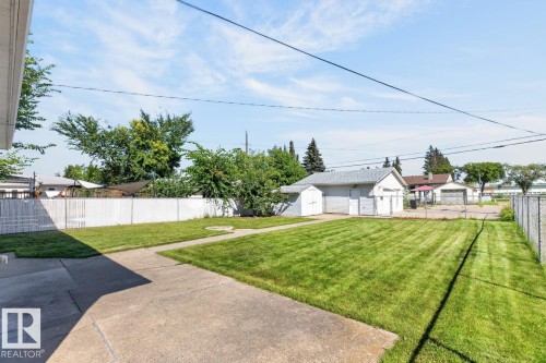Expansive backyard featuring a manicured lawn, concrete patio, and white privacy fencing - 12309 128 Street Nw, Edmonton, AB 