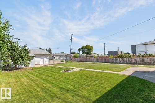 Expansive green lawn with a built-in fire pit, concrete pathways, and a detached garage with a shingled roof - 12309 128 Street Nw, Edmonton, AB 