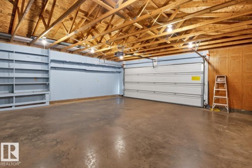 Exposed wood beam ceiling, concrete flooring, built-in shelving, white sectional garage door, and overhead lighting - 12309 128 Street Nw, Edmonton, AB 