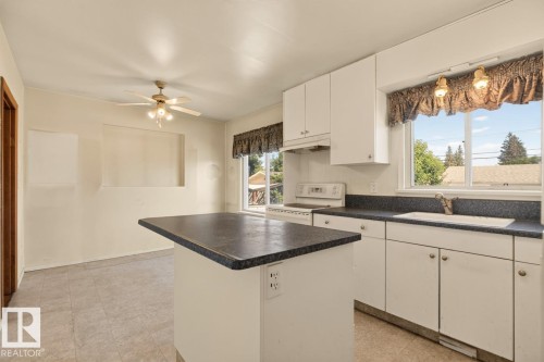 Kitchen featuring white cabinetry, dark countertops, a built-in sink, and a ceiling fan with integrated lighting - 12309 128 Street Nw, Edmonton, AB 