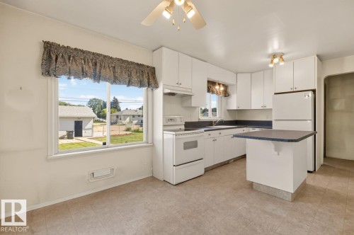 Kitchen featuring white cabinetry, a built-in island, white appliances, and a window overlooking the property - 12309 128 Street Nw, Edmonton, AB 