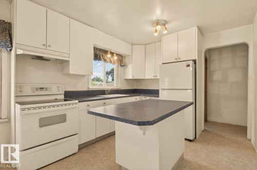 Kitchen featuring white cabinetry, a built-in range, a refrigerator, a center island, and a window above the sink - 12309 128 Street Nw, Edmonton, AB 