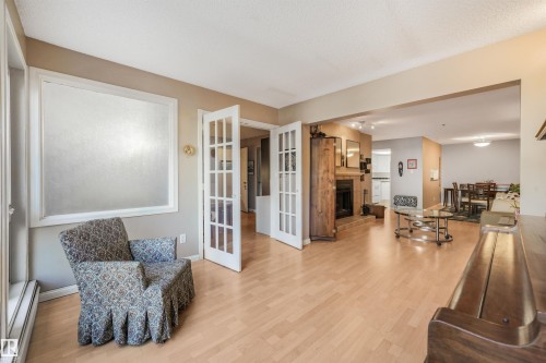 Wood-finish flooring throughout, French doors, recessed lighting, and a built-in fireplace with a stone surround - #203 10171 119 St Nw, Edmonton, AB 