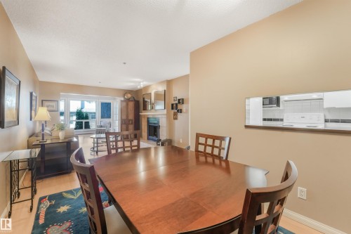 Open-concept living area with wood-finish flooring, a pass-through window, and a built-in fireplace featuring a stone surround - #203 10171 119 St Nw, Edmonton, AB 
