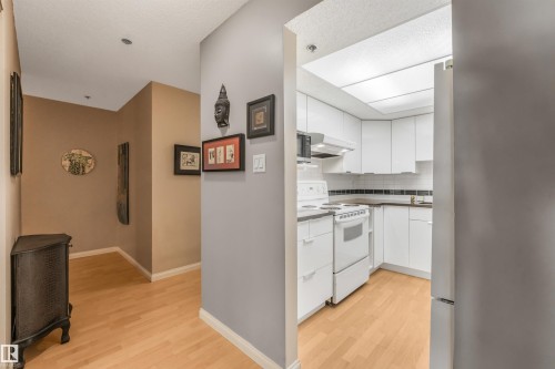 Light wood-finish flooring throughout, recessed lighting, and a kitchen featuring white cabinetry, a white electric range, and a white refrigerator - #203 10171 119 St Nw, Edmonton, AB 