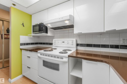 Kitchen featuring white cabinetry, brown countertops, and a white tile backsplash with a black accent strip - #203 10171 119 St Nw, Edmonton, AB 