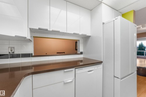 White high-gloss cabinetry, brown solid-surface countertops, integrated dishwasher, white subway tile backsplash, and a pass-through window - #203 10171 119 St Nw, Edmonton, AB 