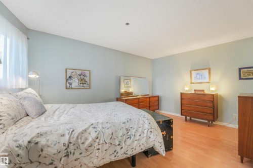 Light wood-finish flooring, light blue wall paint, window with sheer white curtain, built-in ceiling lighting, and wall-mounted sconces - #203 10171 119 St Nw, Edmonton, AB 