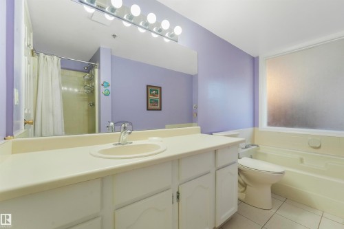 Spacious vanity with an integrated sink and chrome faucet, tile flooring, and a frosted window above the tub - #203 10171 119 St Nw, Edmonton, AB 