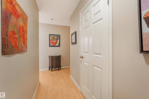 Hallway featuring light wood-finish flooring, neutral wall tones, and white interior doors with brass hardware - #203 10171 119 St Nw, Edmonton, AB 