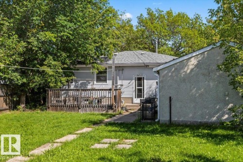 Expansive grassy yard with stepping stones, featuring a wooden deck and a stucco-finished outbuilding - 10990 135 Street Nw, Edmonton, AB 