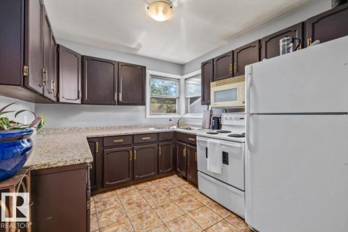 Kitchen featuring dark wood cabinetry, light-toned countertops, tile flooring, and white appliances - 10990 135 Street Nw, Edmonton, AB 