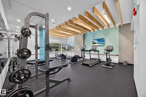 Condo Building Gym Space featuring rubber flooring, ample equipment, and a view of the common area grounds. - #803 10011 123 St Nw, Edmonton, AB 