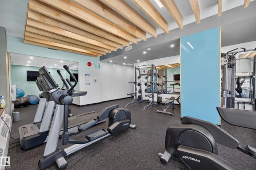 Condo Building Gym Space featuring rubber flooring, ample equipment, and a view of the common area grounds. - #803 10011 123 St Nw, Edmonton, AB 