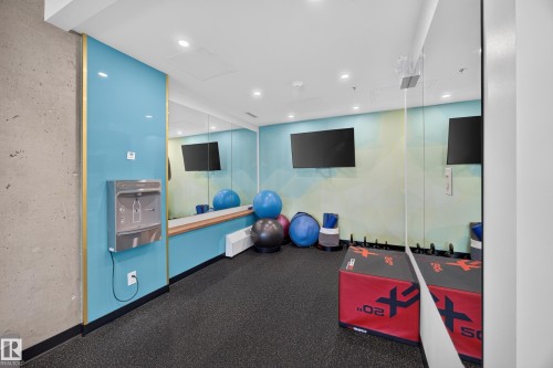 Condo Building Gym Space featuring rubber flooring, ample equipment, and a view of the common area grounds. - #803 10011 123 St Nw, Edmonton, AB 