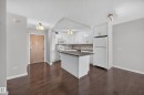 White kitchen featuring quartz counters, hardwood flooring, electric stove, microwave hood fan, space for a dishwasher, and refrigerator. - #803 10011 123 St Nw, Edmonton, AB 