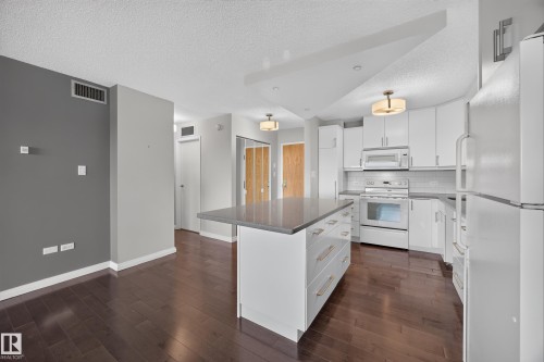 White kitchen featuring quartz counters, hardwood flooring, electric stove, microwave hood fan, space for a dishwasher, and refrigerator. - #803 10011 123 St Nw, Edmonton, AB 