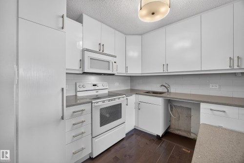White kitchen featuring quartz counters, hardwood flooring, electric stove, microwave hood fan, space for a dishwasher, and refrigerator. - #803 10011 123 St Nw, Edmonton, AB 