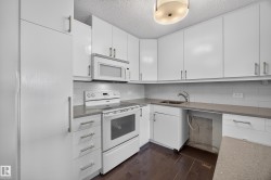 White kitchen featuring quartz counters, hardwood flooring, electric stove, microwave hood fan, space for a dishwasher, and refrigerator. - 