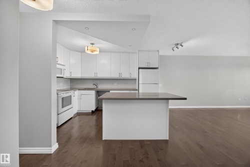 White kitchen featuring quartz counters, hardwood flooring, electric stove, microwave hood fan, space for a dishwasher, and refrigerator. - #803 10011 123 St Nw, Edmonton, AB 