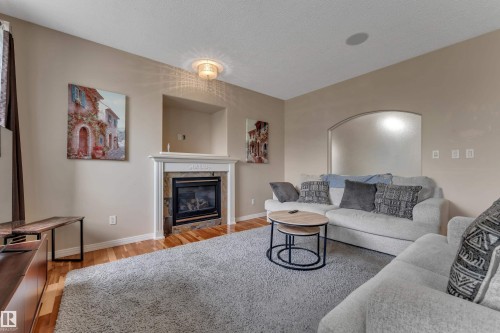 Hardwood flooring, fireplace with stone surround, ornate mantel, recessed wall niche, and arched wall opening - 1226 Mcallister Way Sw, Edmonton, AB 