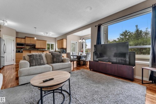 Open-concept living area with wood-finish flooring, a large picture window, and recessed lighting - 1226 Mcallister Way Sw, Edmonton, AB 