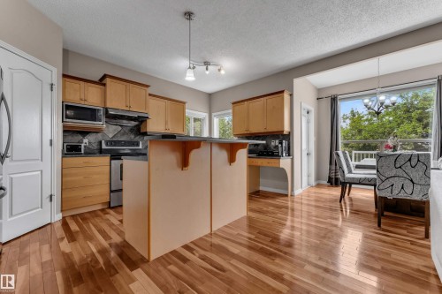 Kitchen and dining area featuring wood-finish flooring, light-toned cabinetry, stainless steel appliances, and a built-in kitchen island - 1226 Mcallister Way Sw, Edmonton, AB 