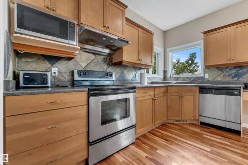 Kitchen featuring wood cabinetry, stainless steel appliances, dark countertops, and a tiled backsplash - 1226 Mcallister Way Sw, Edmonton, AB 