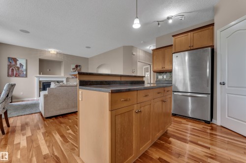 Kitchen island with integrated breakfast bar, wood-finish cabinetry, stainless steel refrigerator, and wood-finish flooring - 1226 Mcallister Way Sw, Edmonton, AB 