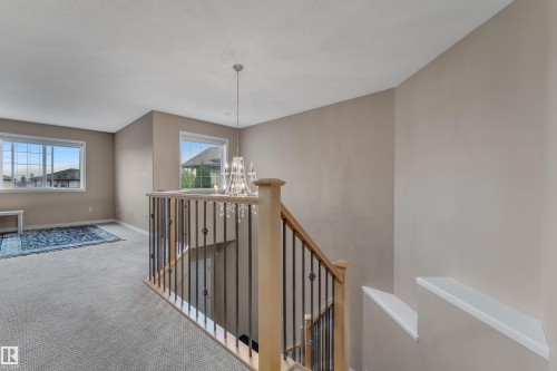 Carpeted landing with a crystal-adorned chandelier, wood banister, and wrought iron spindles - 1226 Mcallister Way Sw, Edmonton, AB 