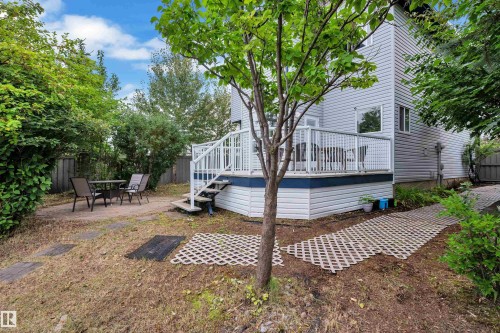 Rear exterior featuring a raised deck with white railing, light gray siding, and a paved patio area - 1226 Mcallister Way Sw, Edmonton, AB 