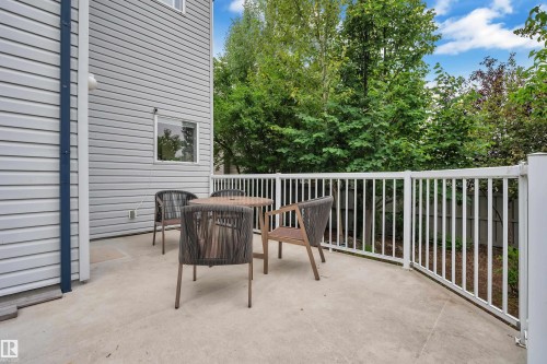Private patio space with a white railing and privacy screening provided by mature trees - 1226 Mcallister Way Sw, Edmonton, AB 