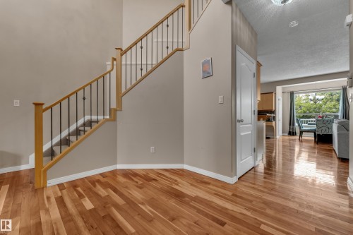 Hardwood flooring throughout the entry, staircase with wooden handrail and black metal balusters, and a white paneled door - 1226 Mcallister Way Sw, Edmonton, AB 