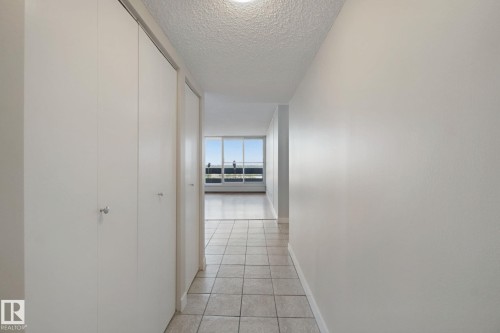 Hallway with light-toned tile flooring, white walls, and built-in closet doors - #104 8745 165 St Nw, Edmonton, AB 