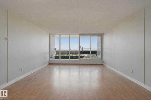 Expansive room featuring wood-finish flooring, white baseboards, and a large window with a distant landscape - #104 8745 165 St Nw, Edmonton, AB 
