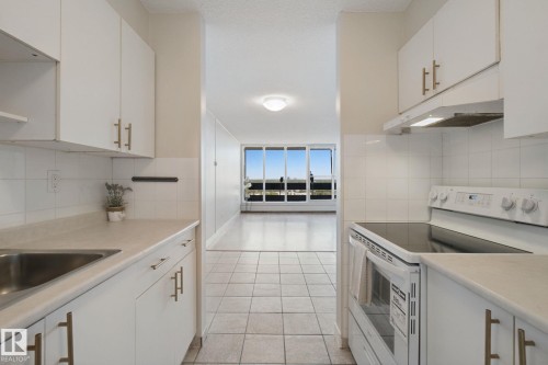 Kitchen featuring white cabinetry with gold-tone hardware, white tiled backsplash, and light-toned countertops - #104 8745 165 St Nw, Edmonton, AB 