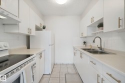 White cabinetry with gold-tone hardware, white tile backsplash, dual basin stainless steel sink, and light-toned countertops - 