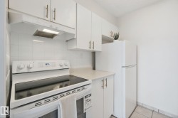 White cabinetry with gold-finish hardware, white tile backsplash, contemporary electric range, and light-tone countertops - 