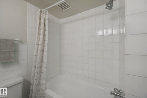 Bathtub with white tile surround, chrome shower fixtures, and an overhead ventilation fan - #104 8745 165 St Nw, Edmonton, AB 