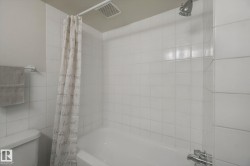 Bathtub with white tile surround, chrome shower fixtures, and an overhead ventilation fan - 