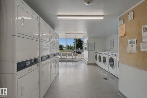 Well-lit laundry facility with multiple commercial-grade washers and dryers, resilient flooring, and ample natural light - #104 8745 165 St Nw, Edmonton, AB 