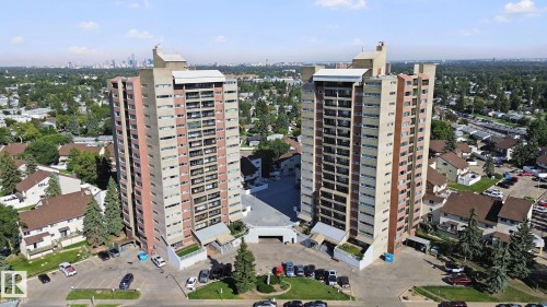 Two high-rise buildings featuring multiple balconies, surrounded by paved parking areas and mature trees - #104 8745 165 St Nw, Edmonton, AB 