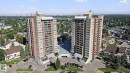 Two high-rise buildings featuring multiple balconies, surrounded by paved parking areas and mature trees - #104 8745 165 St Nw, Edmonton, AB 