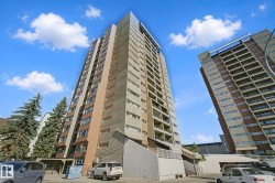 Multi-story high-rise building with a mixed material facade, featuring balconies and an integrated ground-level parking area - 