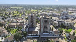 Two high-rise structures featuring multiple balconies, surrounded by various residential buildings and expansive green spaces - 