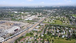 Expansive aerial perspective showcasing a residential neighborhood, commercial developments, and an elevated transit line - 
