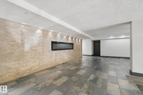 Stone tile flooring with varied rectangular patterns, stone accent wall, recessed lighting, linear electric fireplace, and dark-paneled door - #104 8745 165 St Nw, Edmonton, AB 