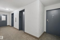Carpeted hallway featuring two elevators and a property entry door - 
