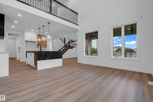Open-concept living area featuring high ceilings, wood-finish flooring, and a contemporary kitchen island with a dark countertop - 57 Meadowgrove Lane, Spruce Grove, AB - Indoor